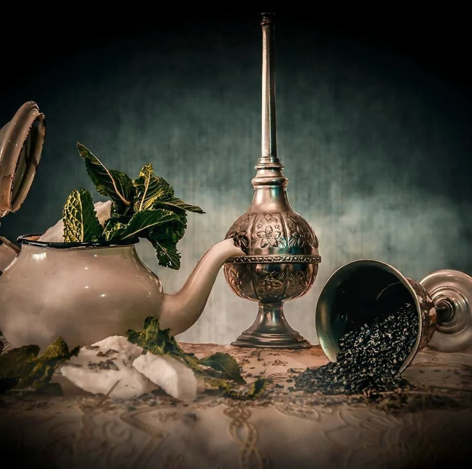 Teiera marocchina, foglie di menta fresca, zucchero in zollette e tè verde sfuso in un bicchiere rovesciato